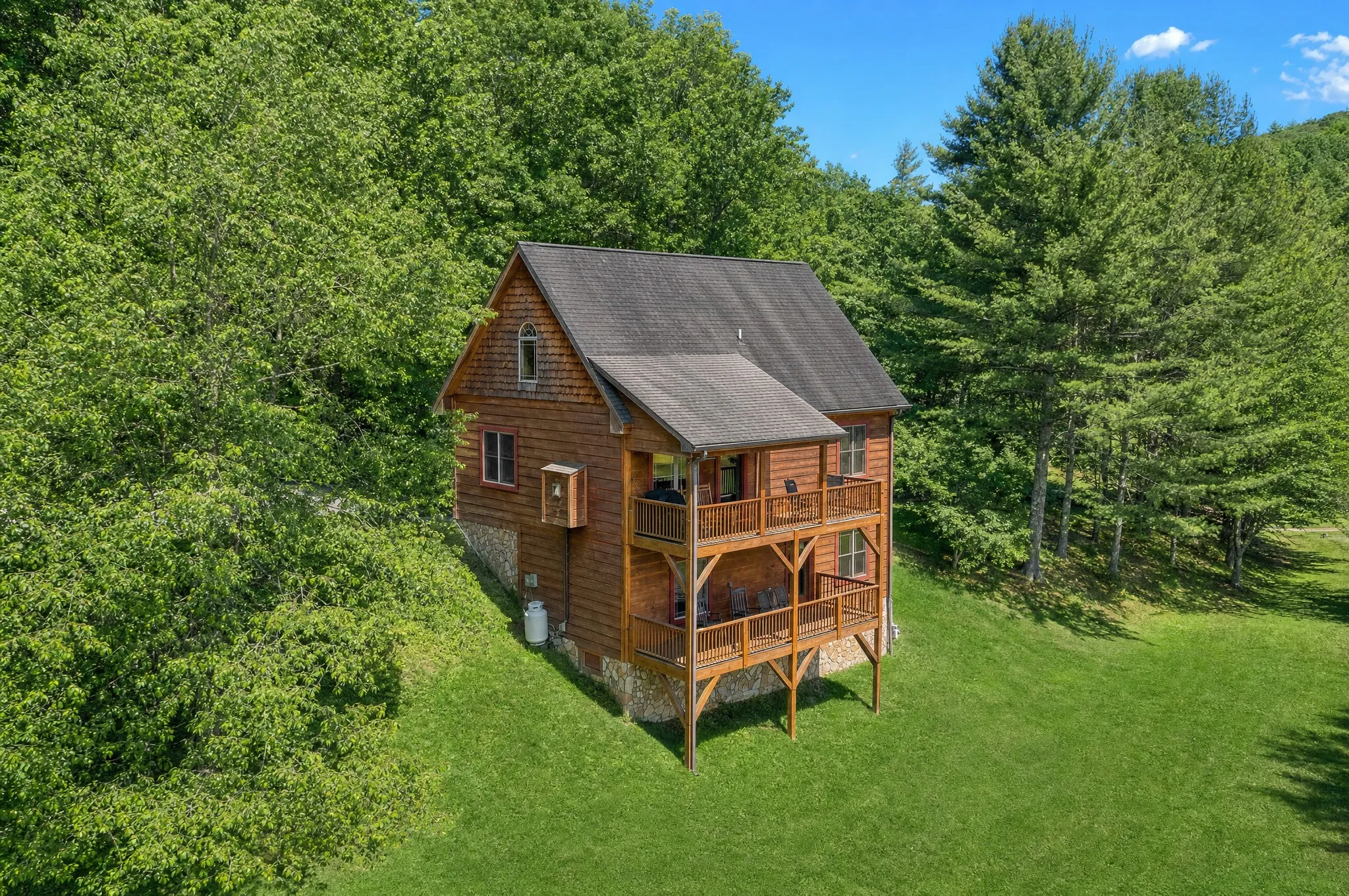 The cedar-shake cabin in summer with its stacked two-level deck facing the lawn