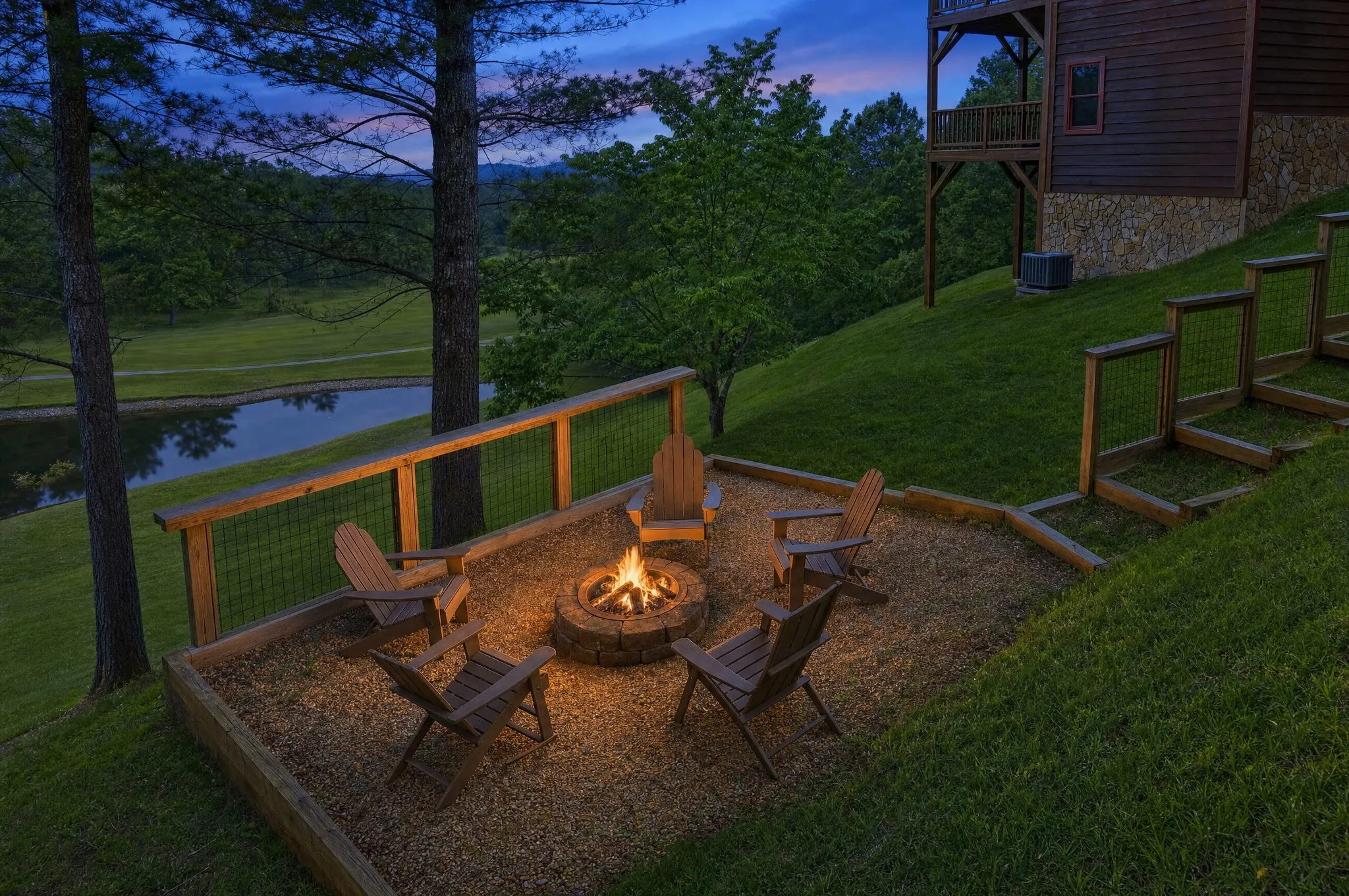 Lit fire pit ringed by Adirondack chairs at dusk, the golf-course pond and Blue Ridge mountains beyond