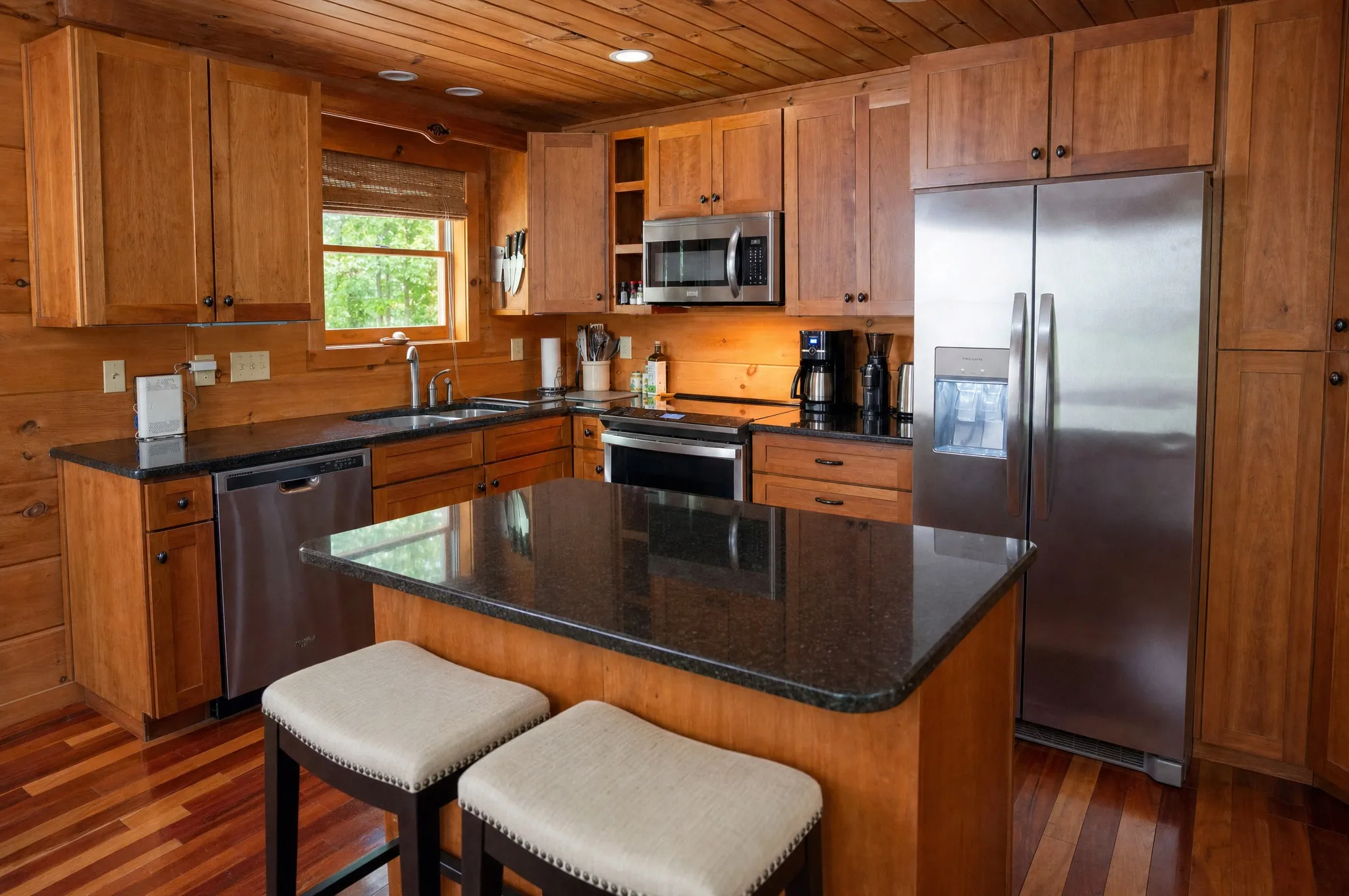 Cabin kitchen with a granite-topped island, bar stools, and stainless steel appliances